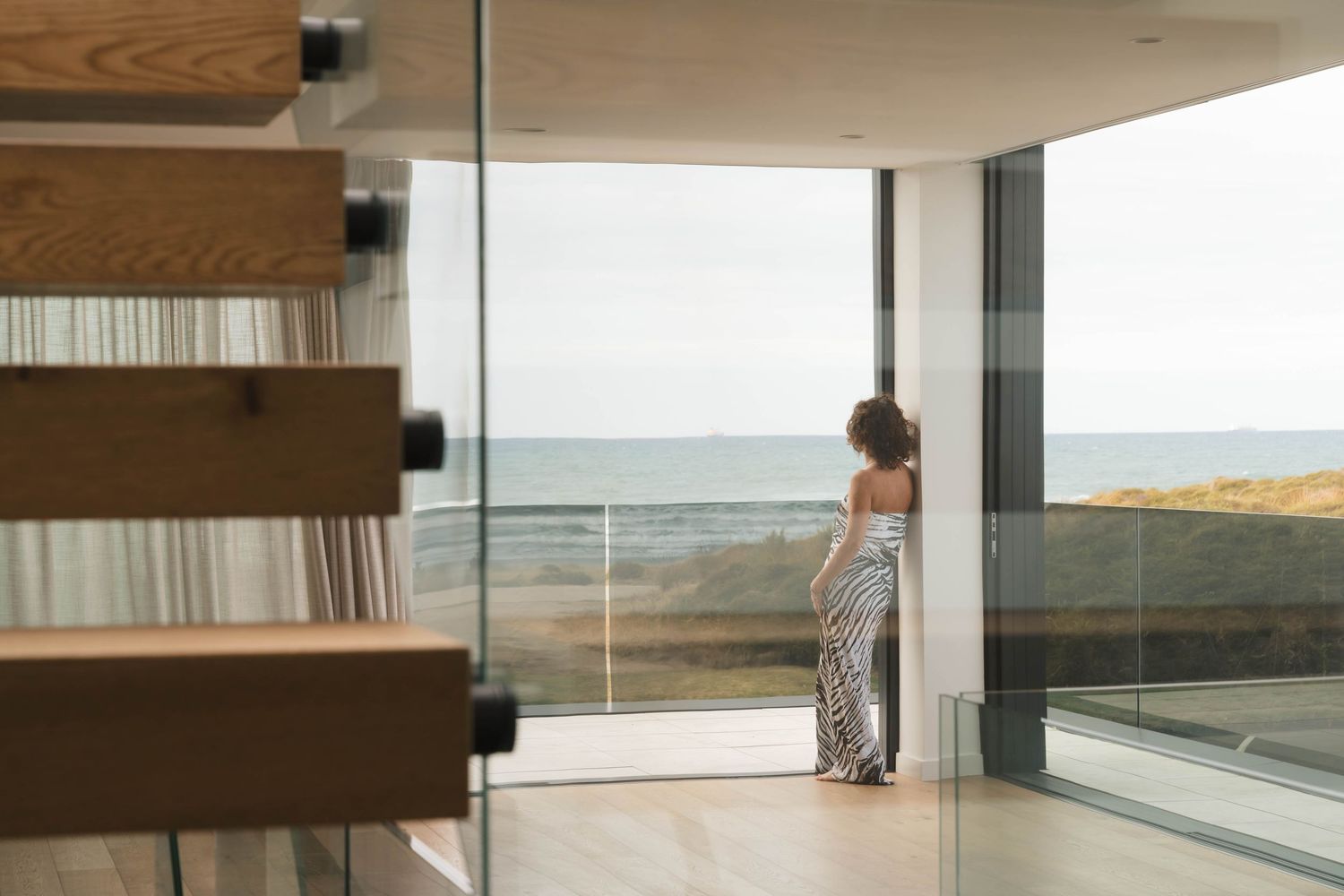 Minimalist interior with wood beams and large windows overlooking coastal landscape.