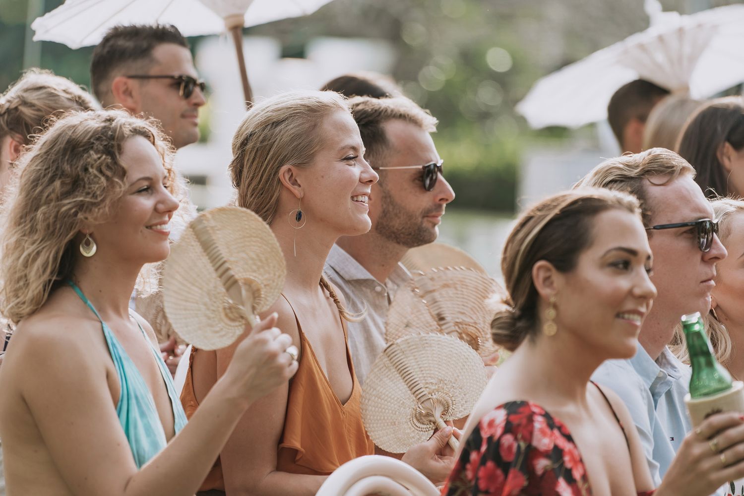 Wedding guests holding white parasols while enjoying an outdoor celebration.