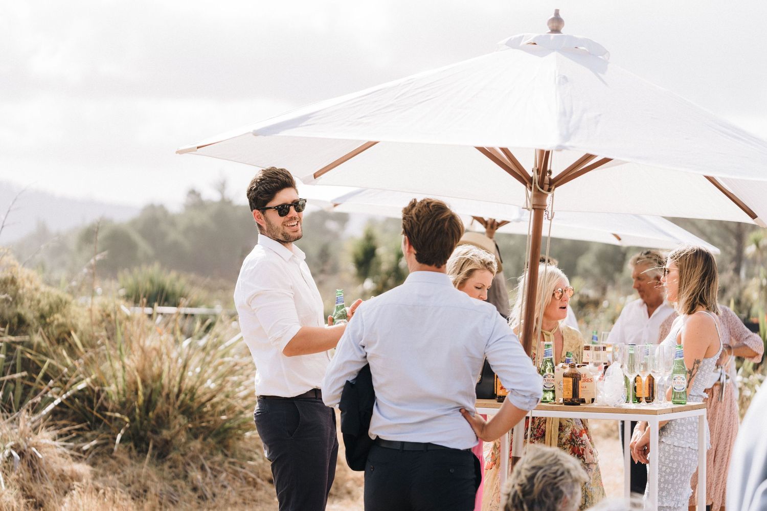 Casual outdoor reception gathering under white umbrellas with coastal views.