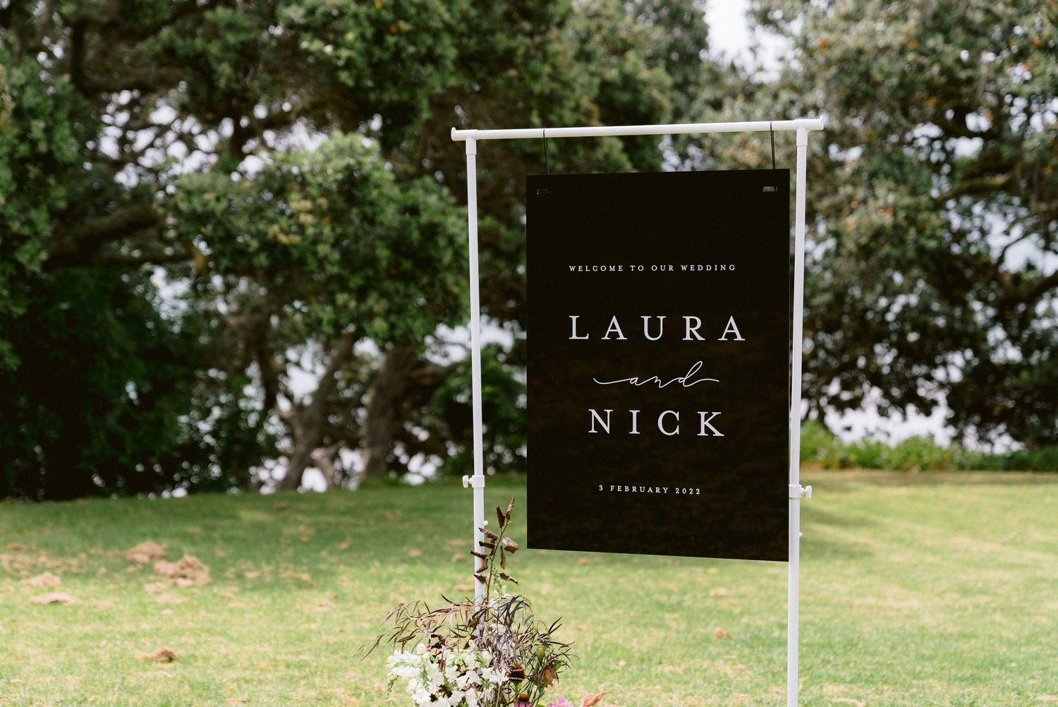 White wedding arch decorated with delicate wildflowers stands elegantly on a green lawn.