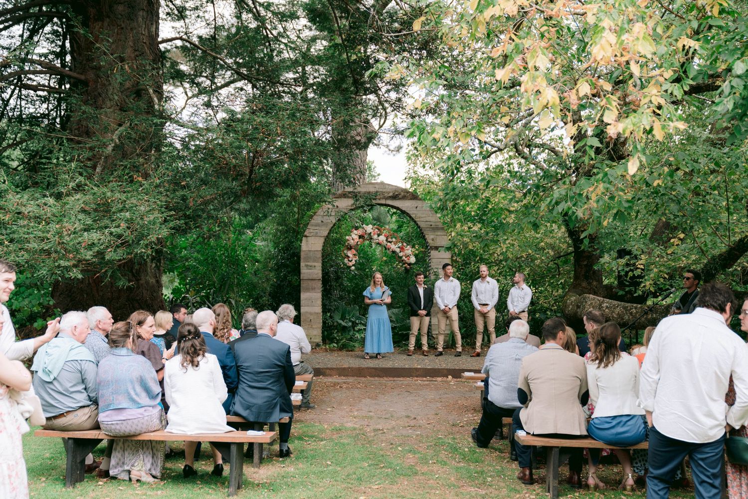 Wedding guests seated at outdoor tables in a garden setting during a reception.