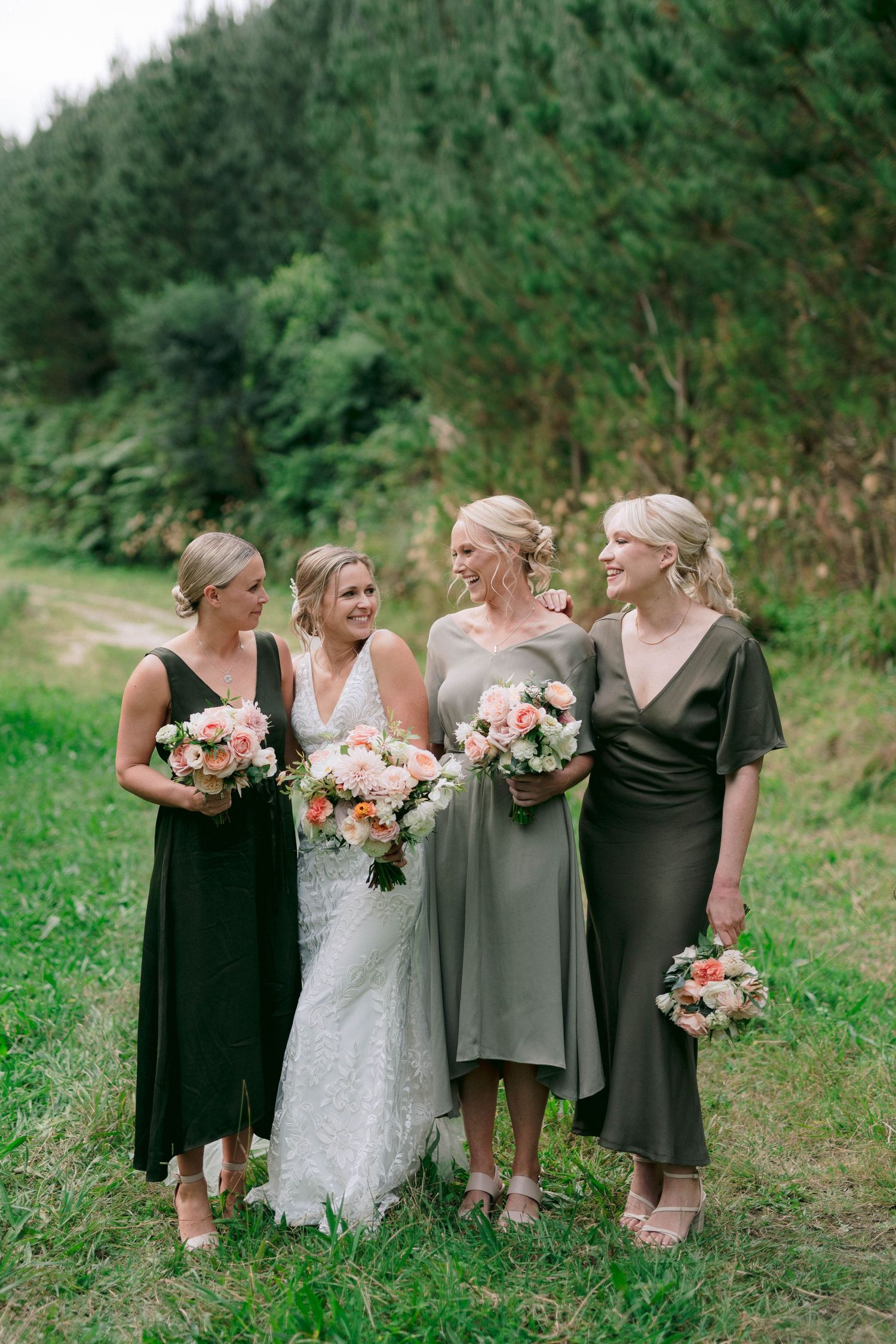 Bridal party in mix of dark and neutral dresses posing together in a grassy field.