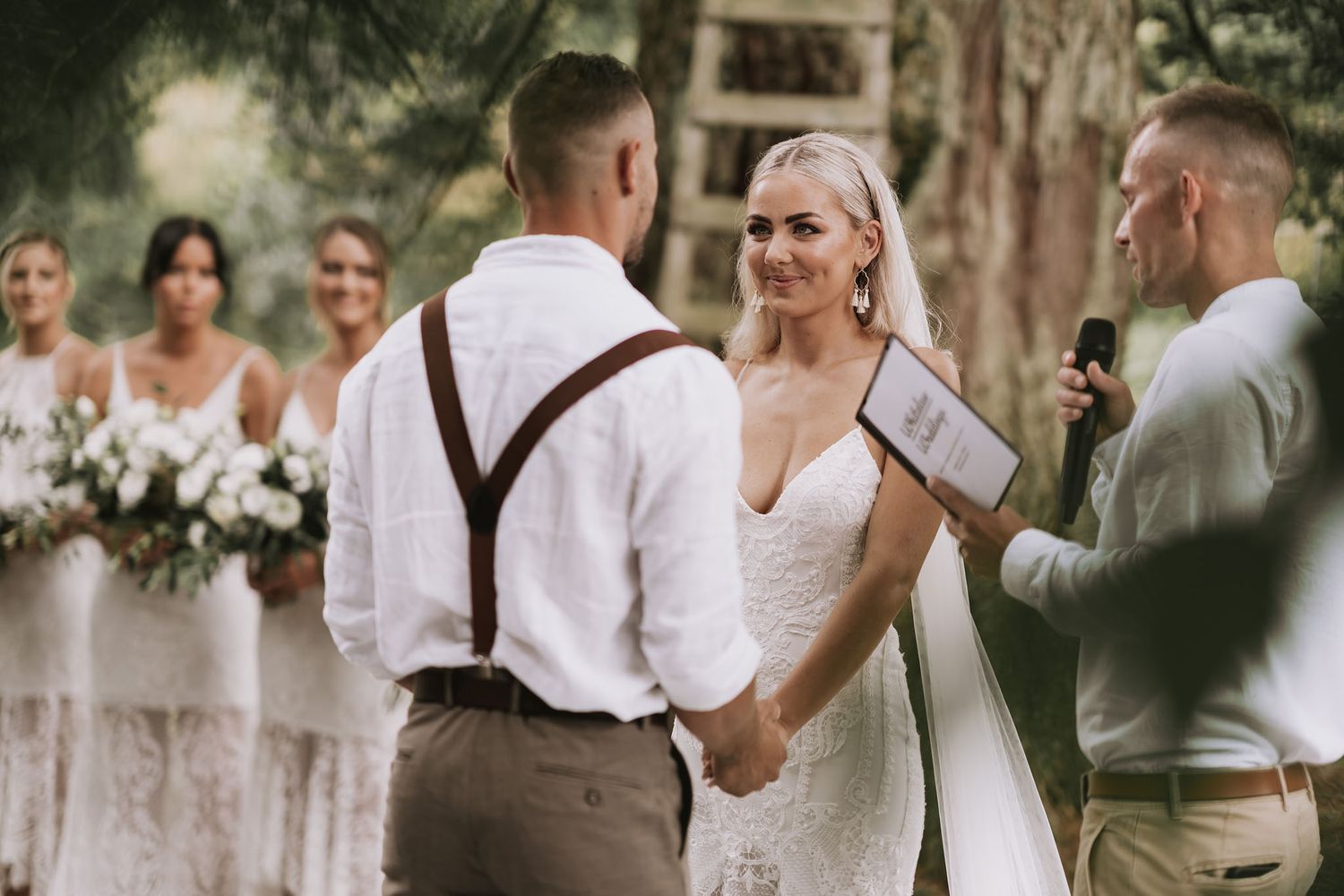 Wedding party members in brown vests and white shirts celebrate outdoors with champagne during a rustic forest ceremony.