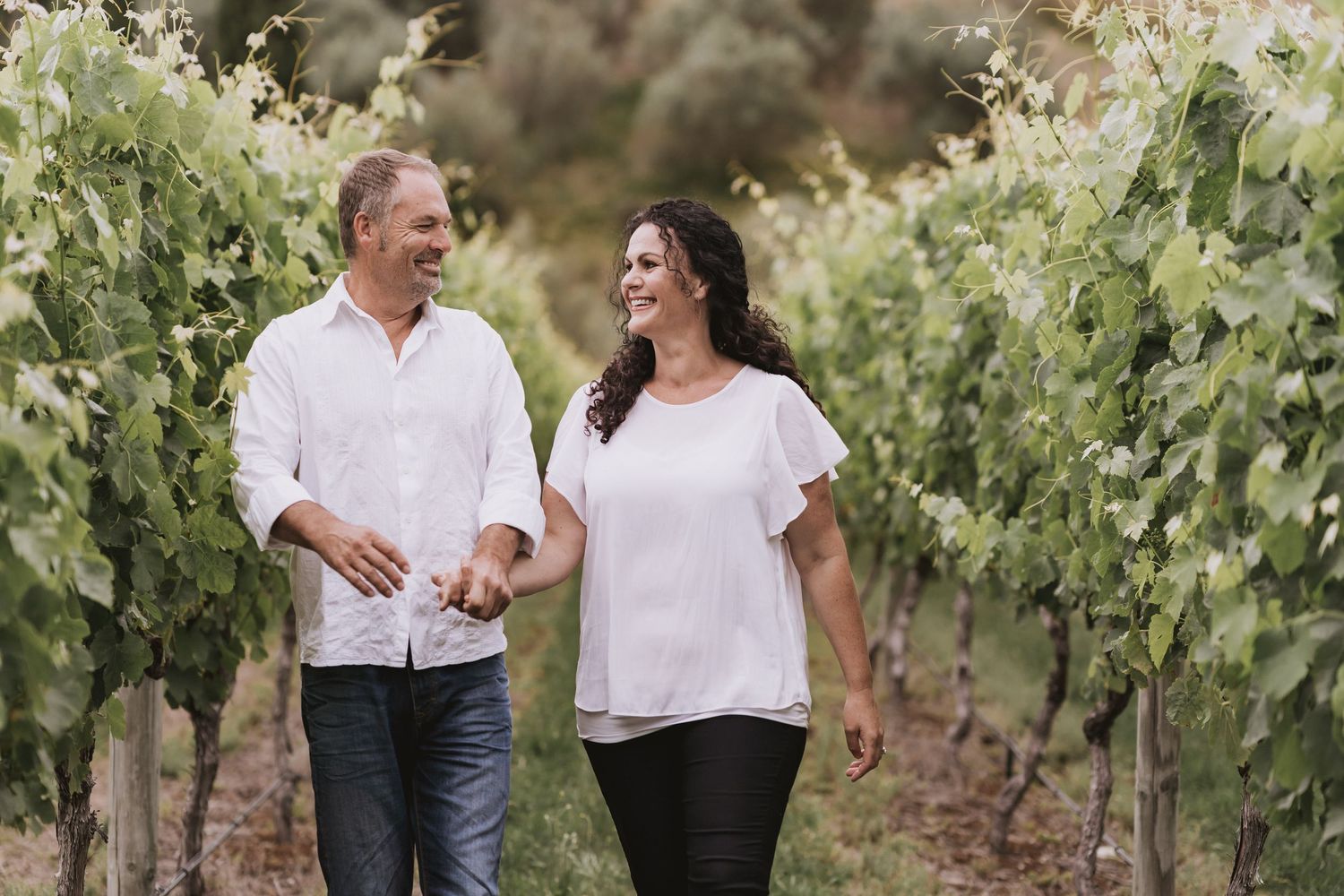 Two people walking together through scenic vineyard rows on a sunny afternoon.