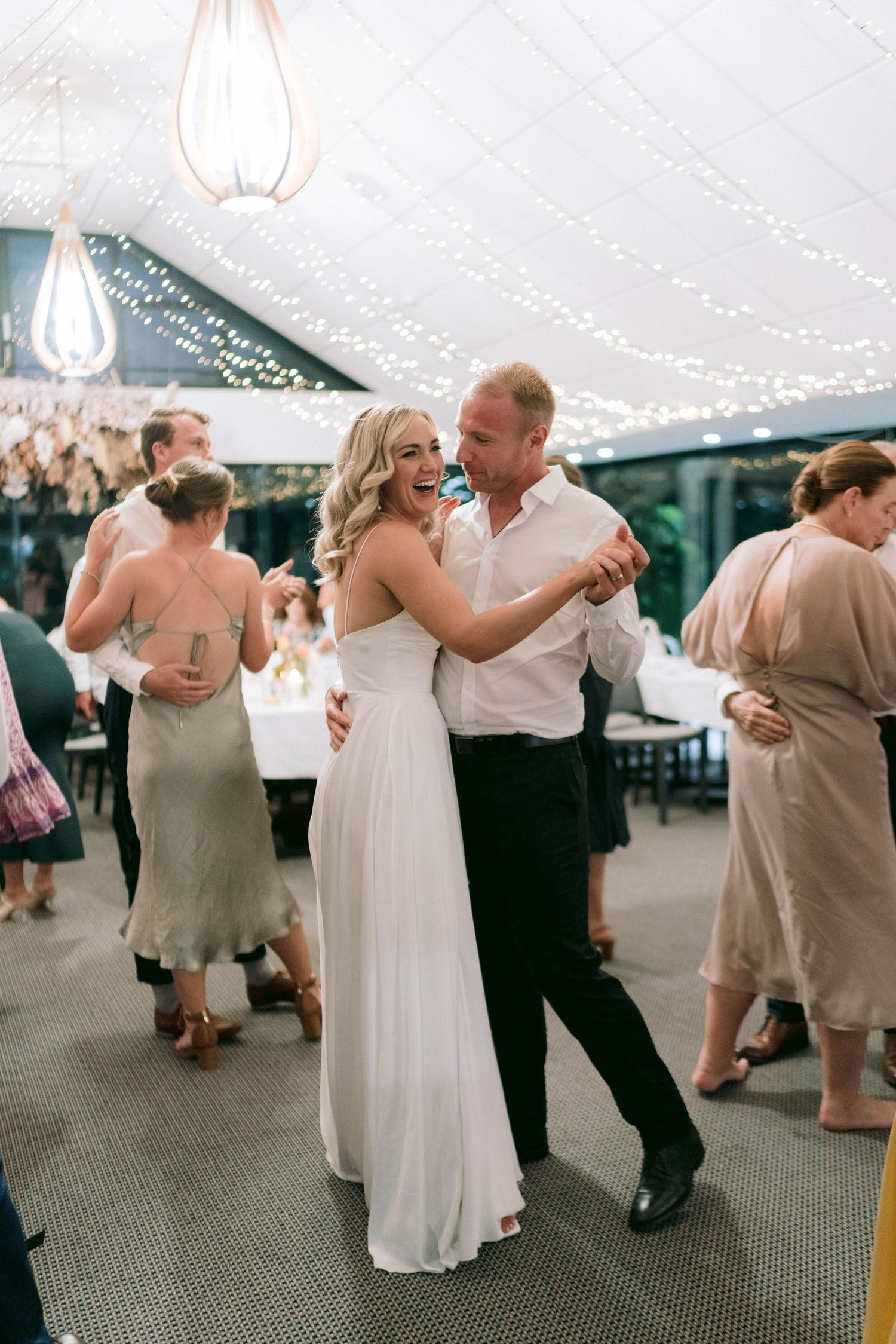 Couple embraces while dancing under twinkling lights at an elegant tented wedding reception.