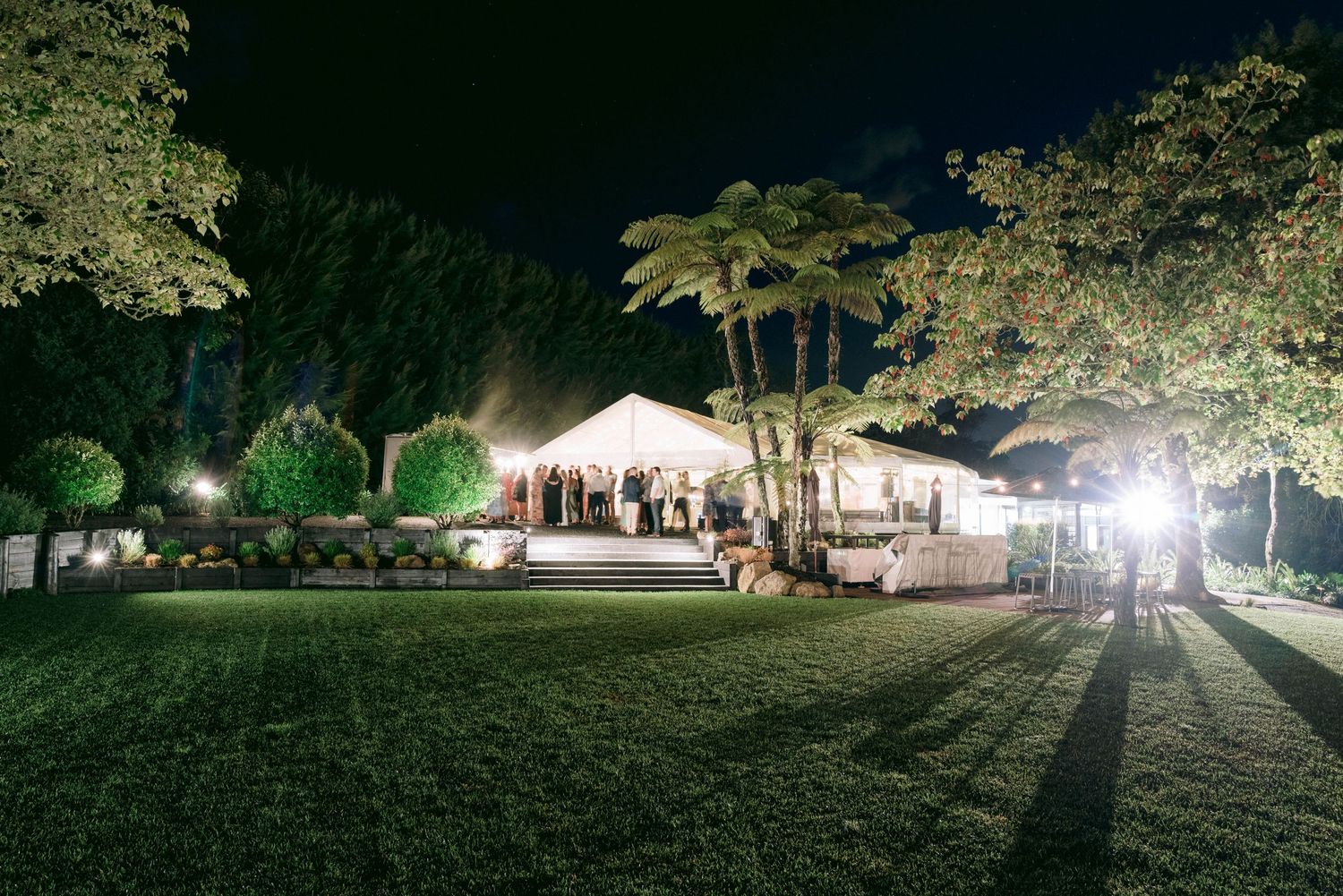 White wedding tent illuminated at night with string lights and trees creating a romantic outdoor reception setting.
