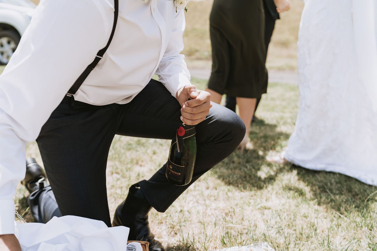 Newlyweds and wedding party recline on grassy lawn during casual outdoor reception celebration.
