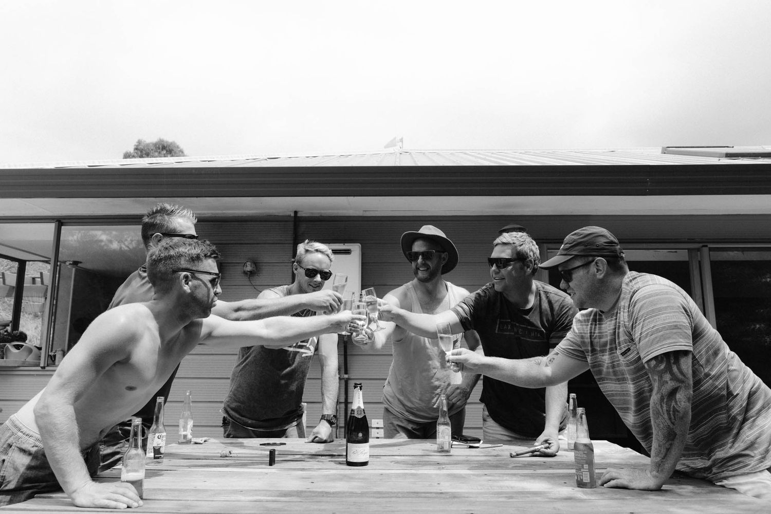 A group toasts with bottles during an outdoor gathering in black and white photography.