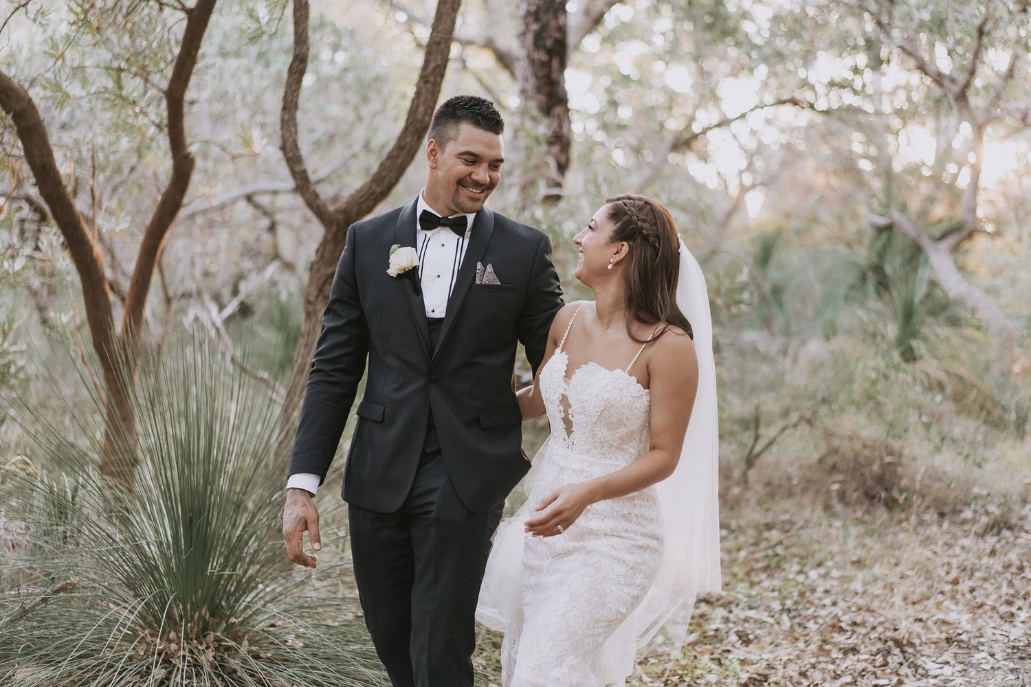 Newlyweds share romantic moments while walking through a scenic outdoor setting in elegant formal wedding attire.