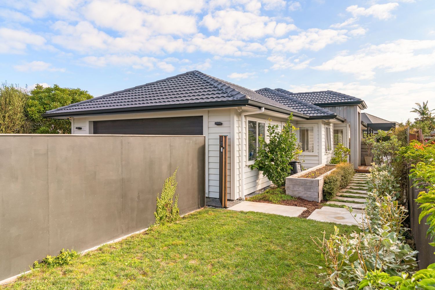 Panoramic view of modern suburban homes with grey tile roofs under partly cloudy blue sky.