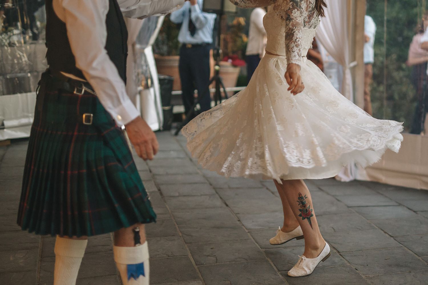 Dancers in kilts and white dresses perform traditional Scottish dance moves on a stone floor during a formal event.