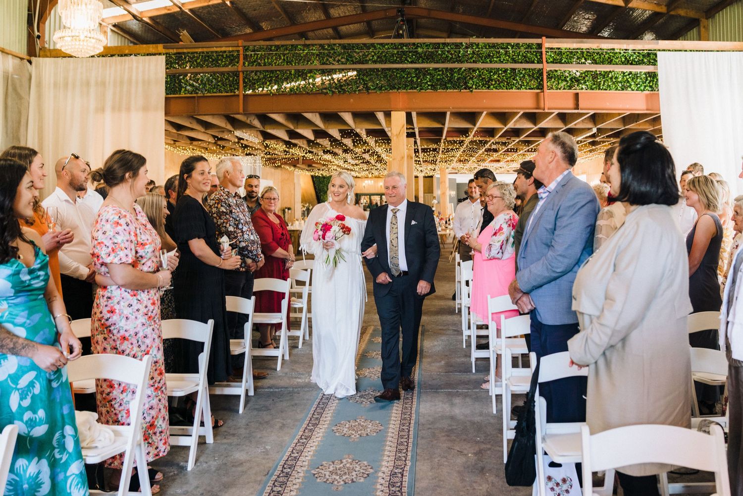Wedding guests mingle and chat in an elegant rustic barn venue with white seating arrangements.
