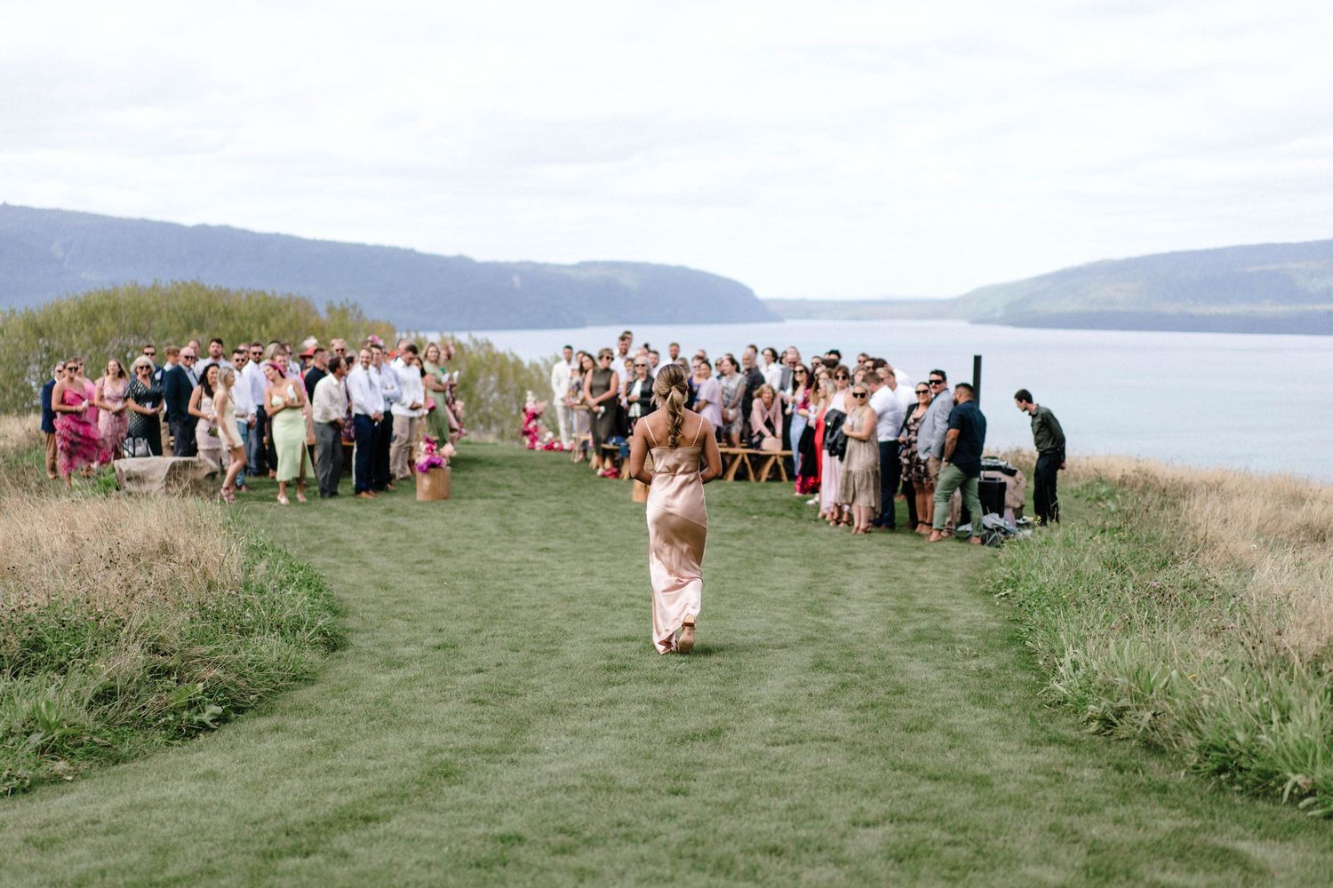 Wedding guests lined up on a grassy path overlooking a scenic coastal view.