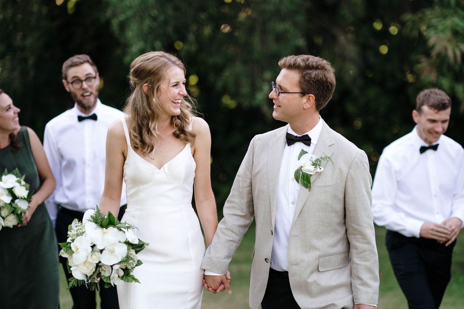 Wedding party in white and ivory formal attire walking together outdoors.