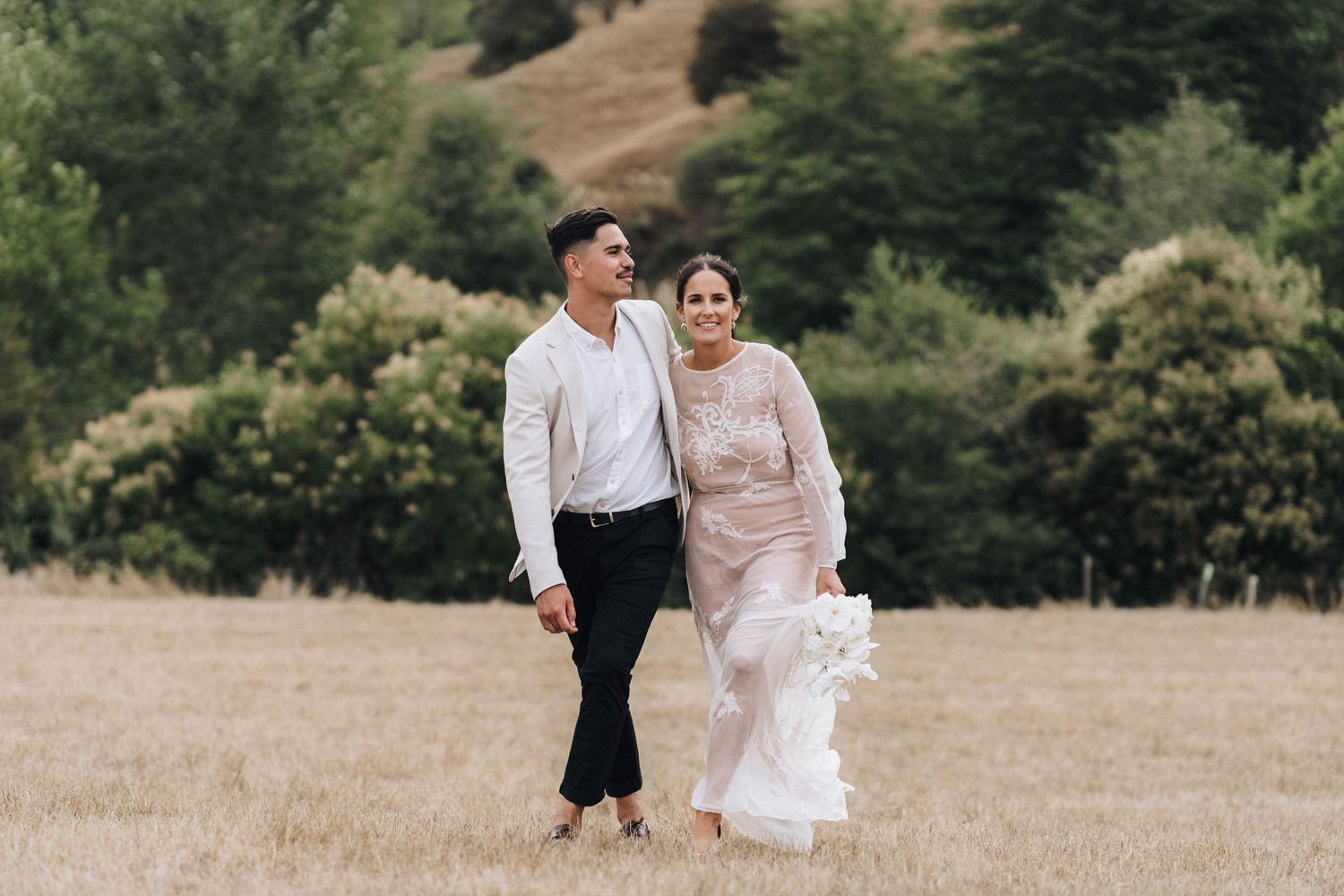 Happy newlyweds walking together through a scenic hillside field.