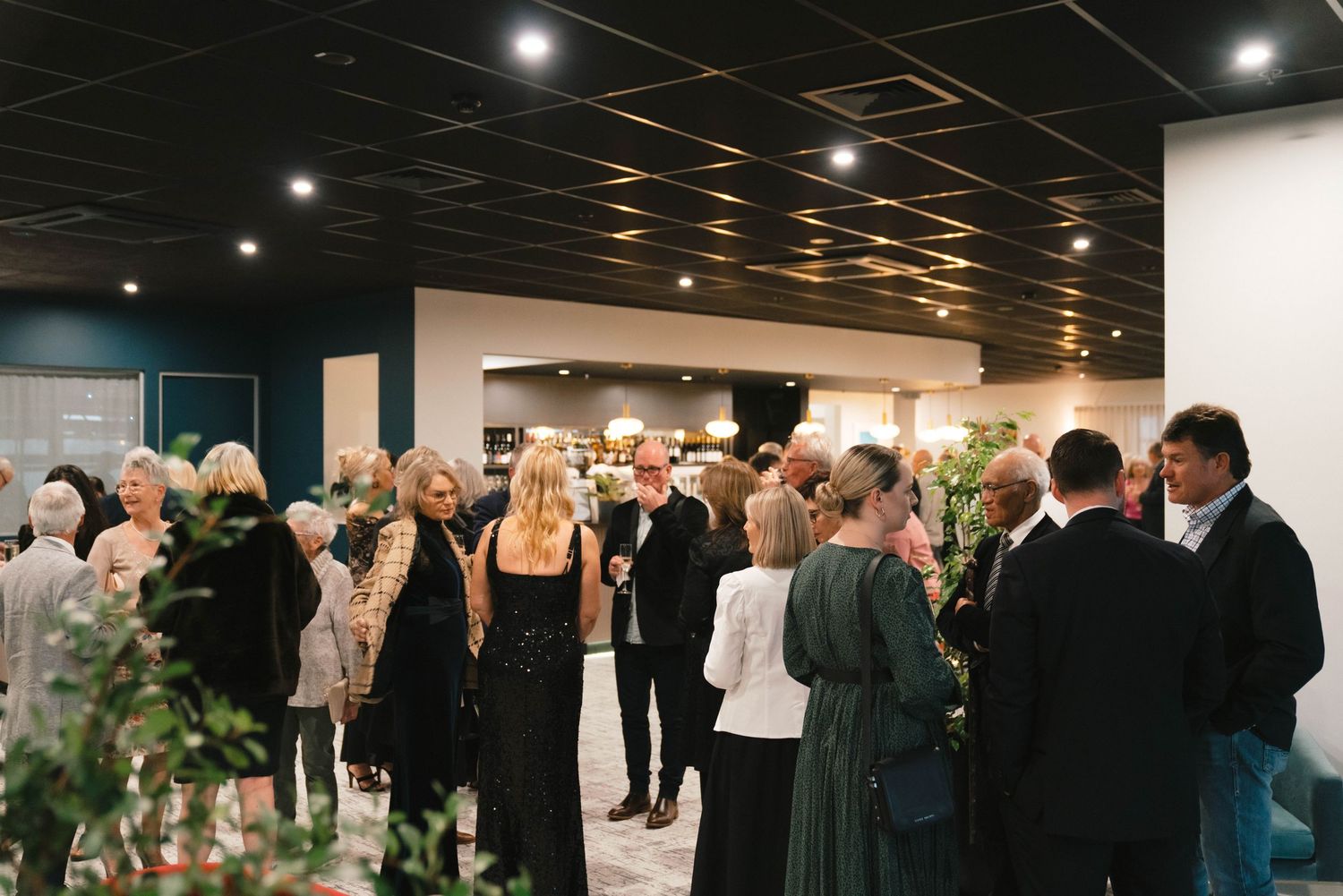 A crowded event space with guests mingling at an indoor reception under modern ceiling lighting.