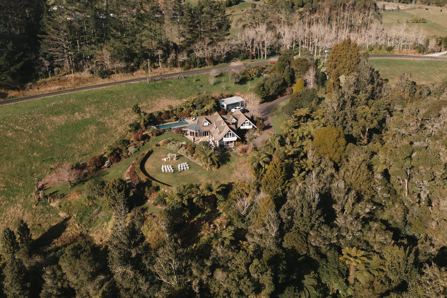 Aerial view of a luxury rural property with swimming pool nestled among trees and rolling hills.