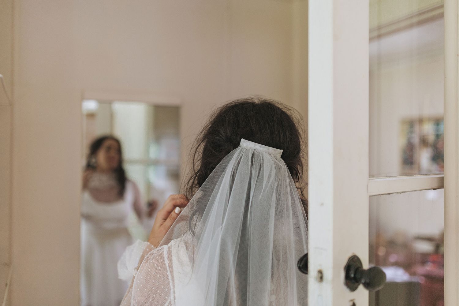 White bridal veil being adjusted in front of a mirror during wedding preparation.
