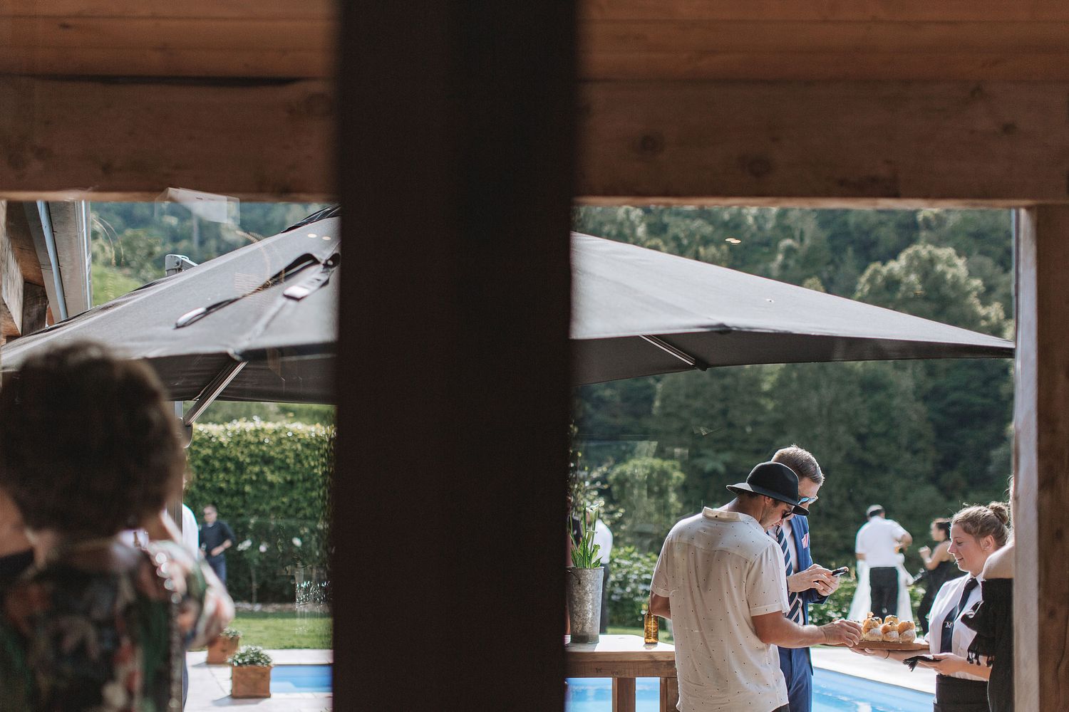 Outdoor event space framed by wooden beams with guests gathering on a sunny afternoon.