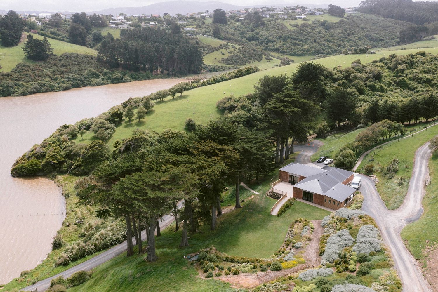 Aerial view of a rural property with buildings nestled along a winding river surrounded by green hills and trees.