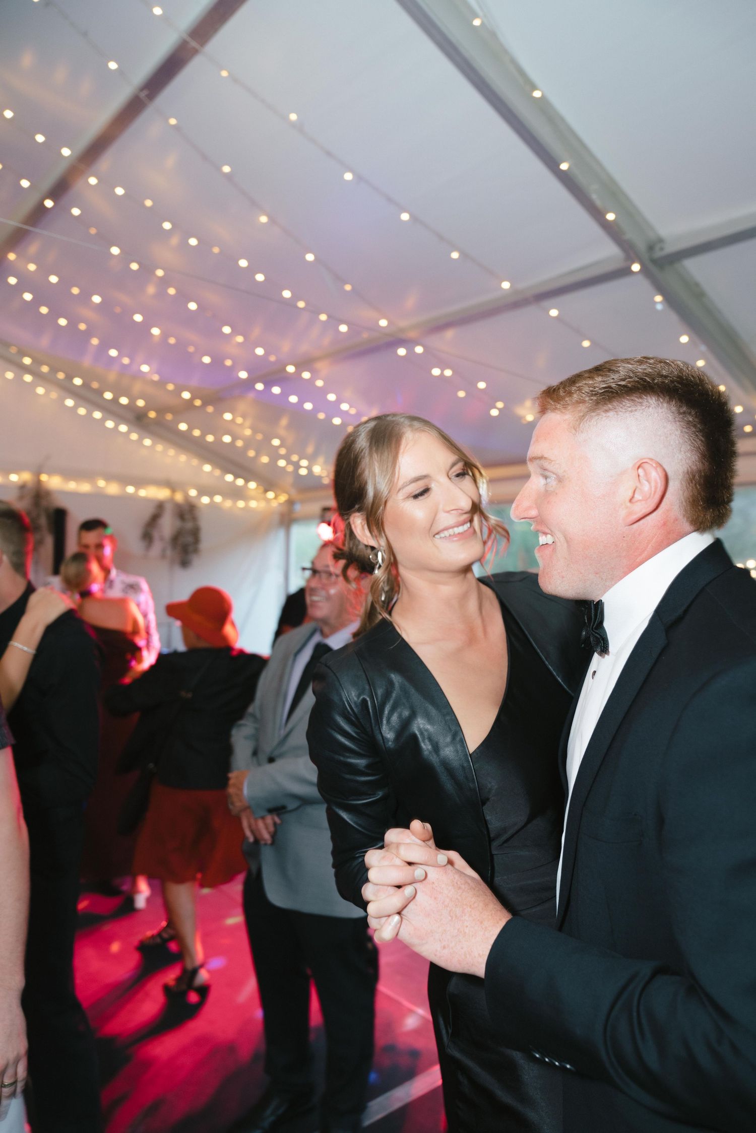 A couple shares an intimate dance moment under string lights at their wedding reception.
