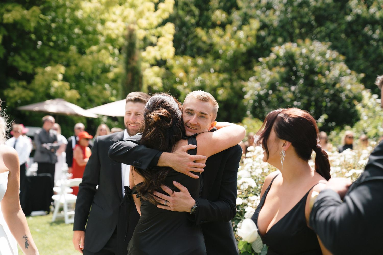 Wedding guests share emotional embraces during an outdoor celebration.