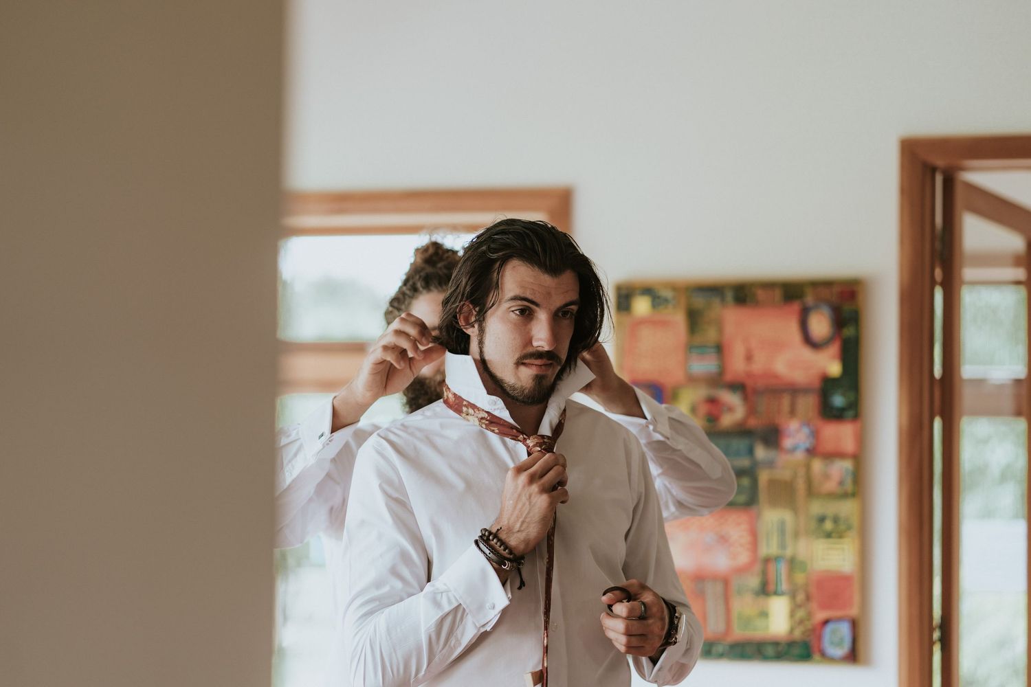 Person wearing white button-down shirt looks in mirror while adjusting sleeves and buttons during morning routine.