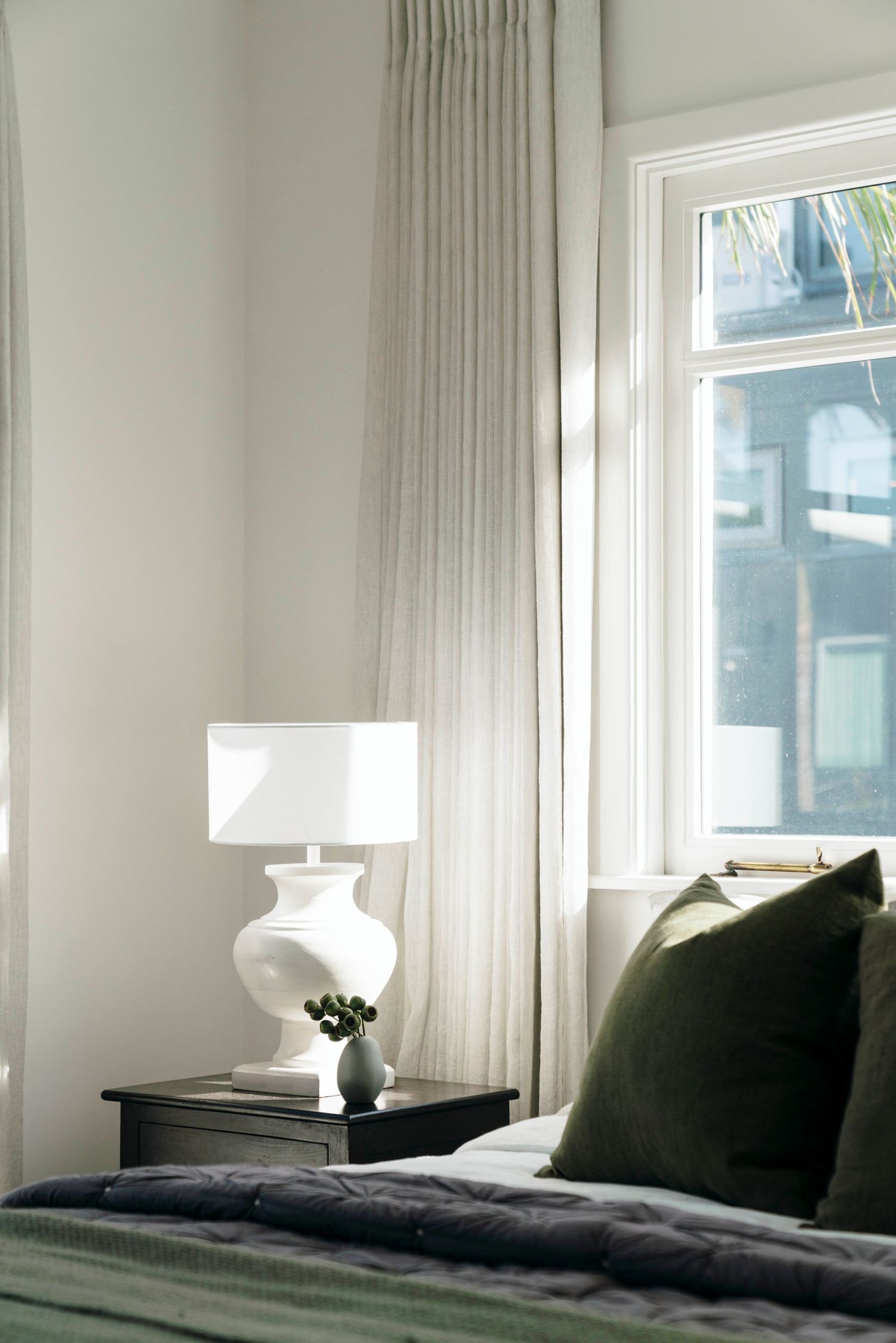 Serene bedroom with white walls, floor-length curtains, and dark accent pillows.