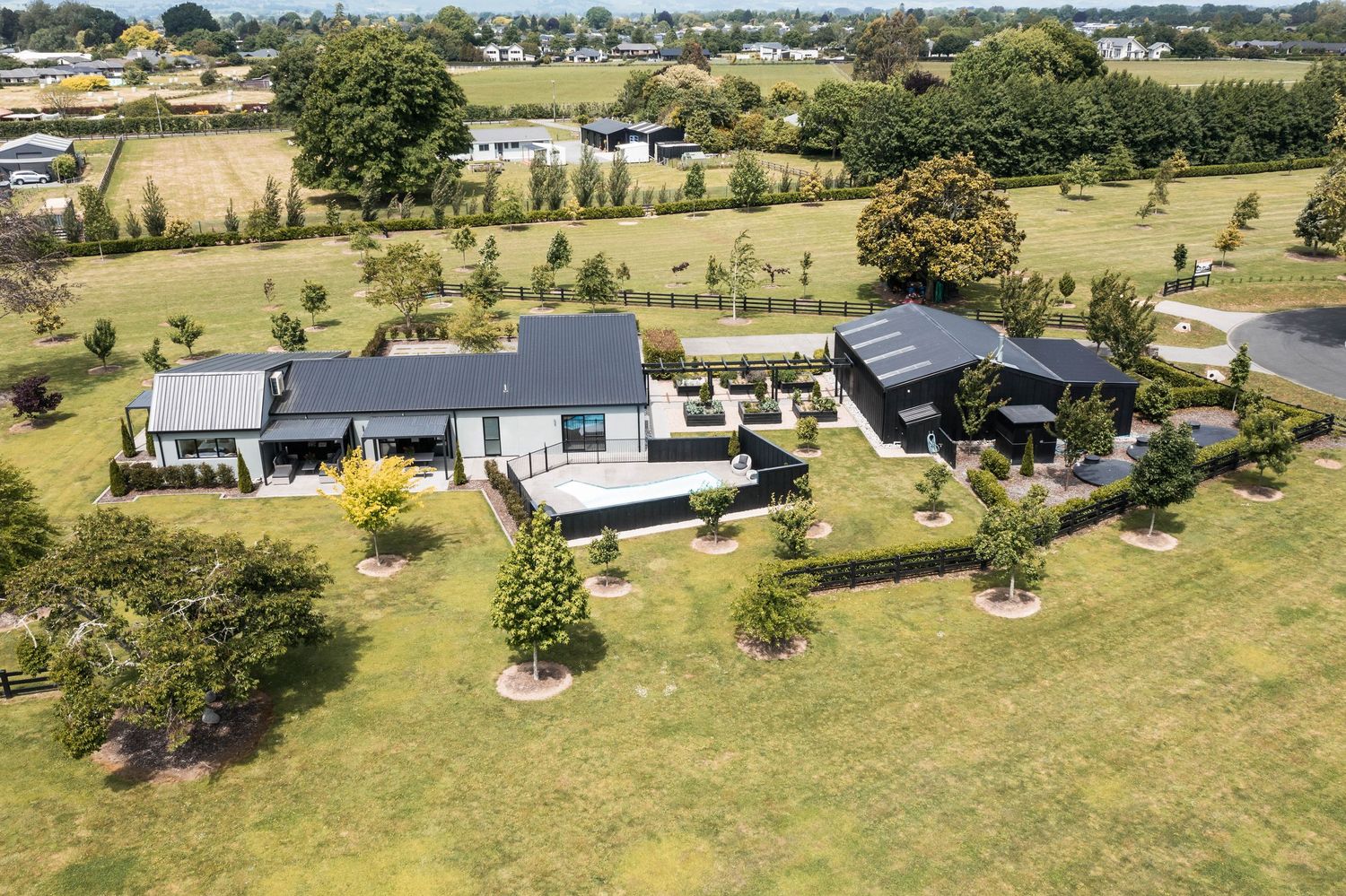 Aerial view of a modern rural property with grey buildings and landscaped gardens on a spacious grassy lot.