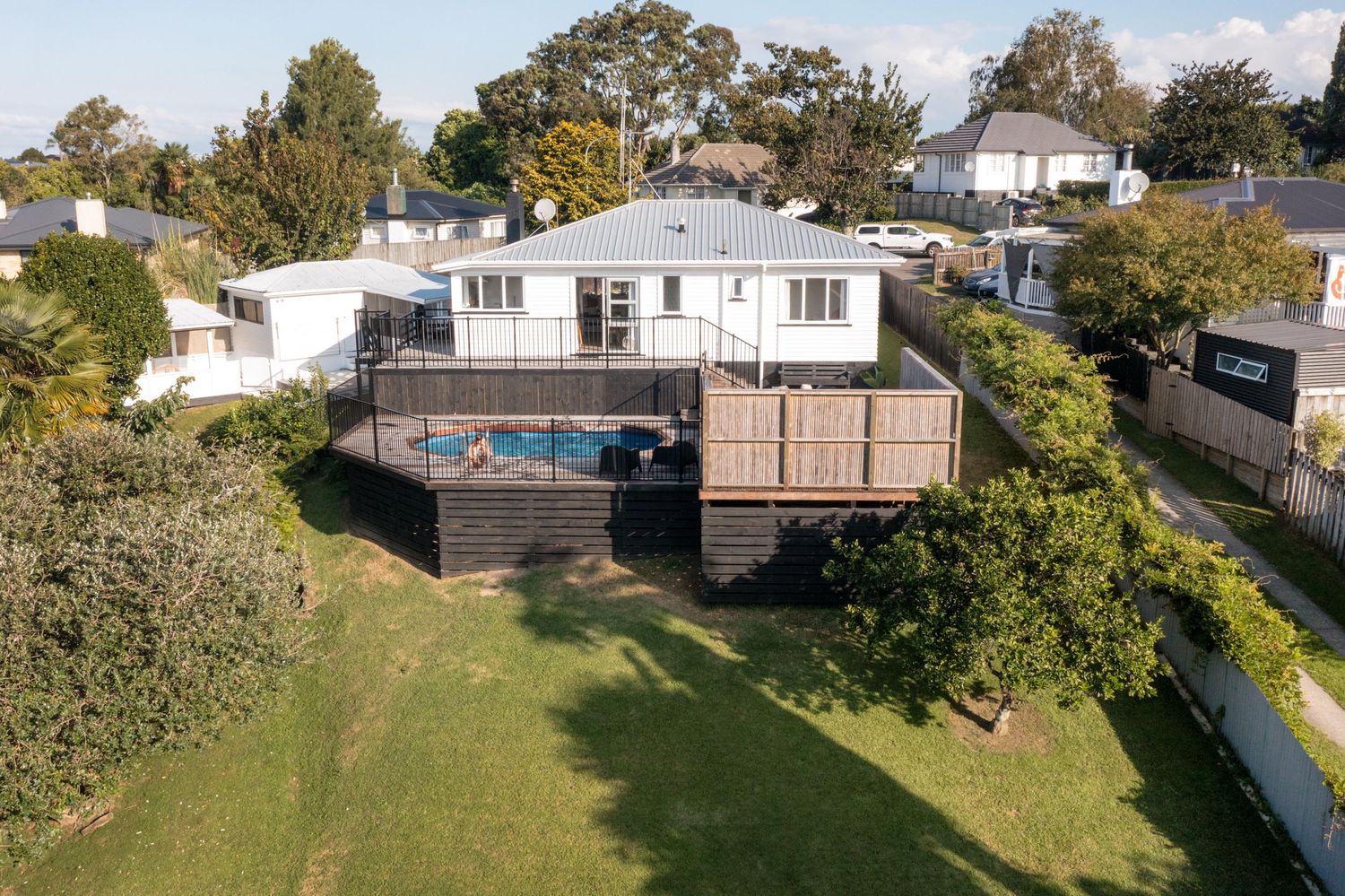 Aerial view of a white suburban house with a spacious backyard surrounded by trees and fencing.
