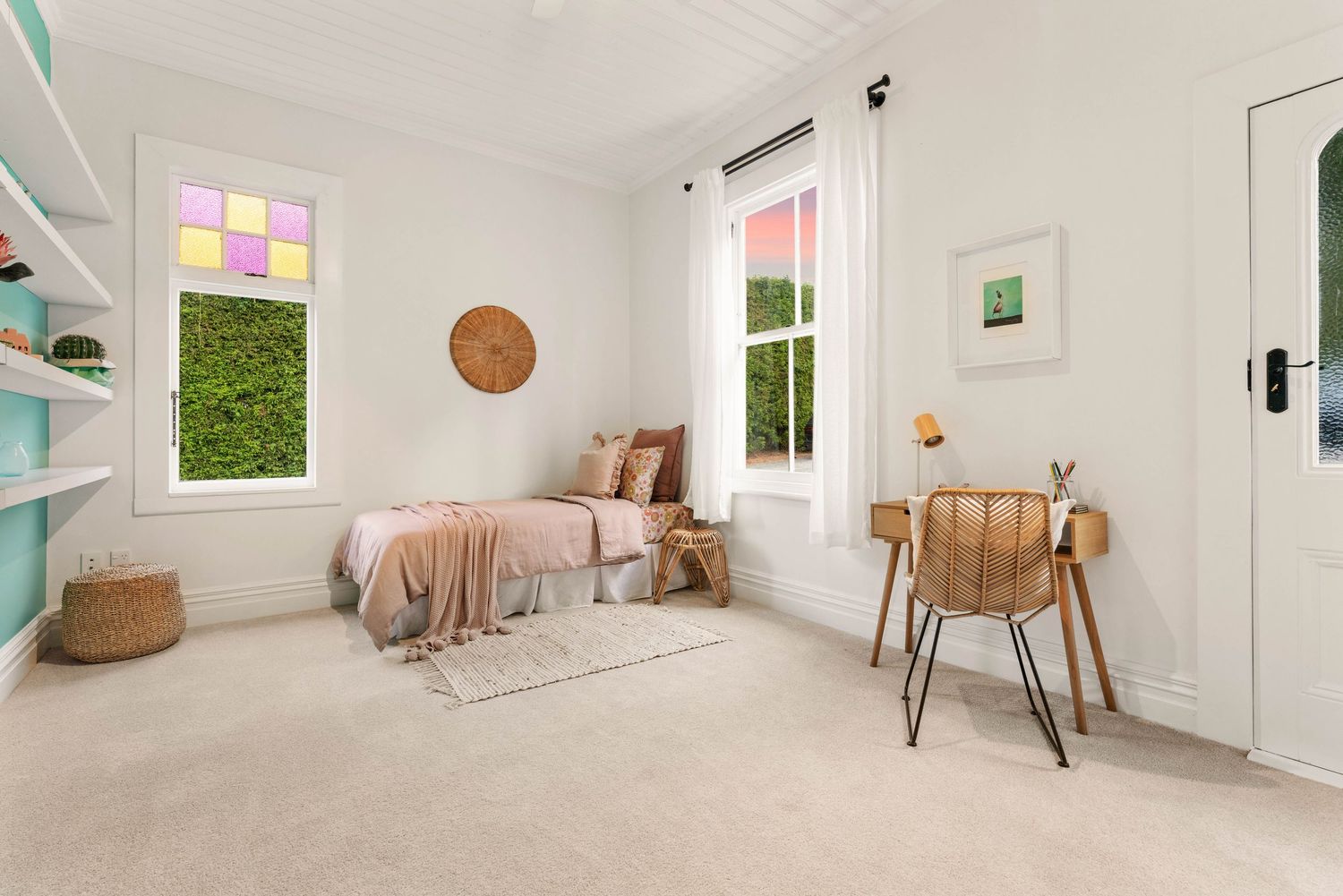 Bright bedroom with pastel decor featuring white walls, mint shelving, pink bedding and natural rattan accents.