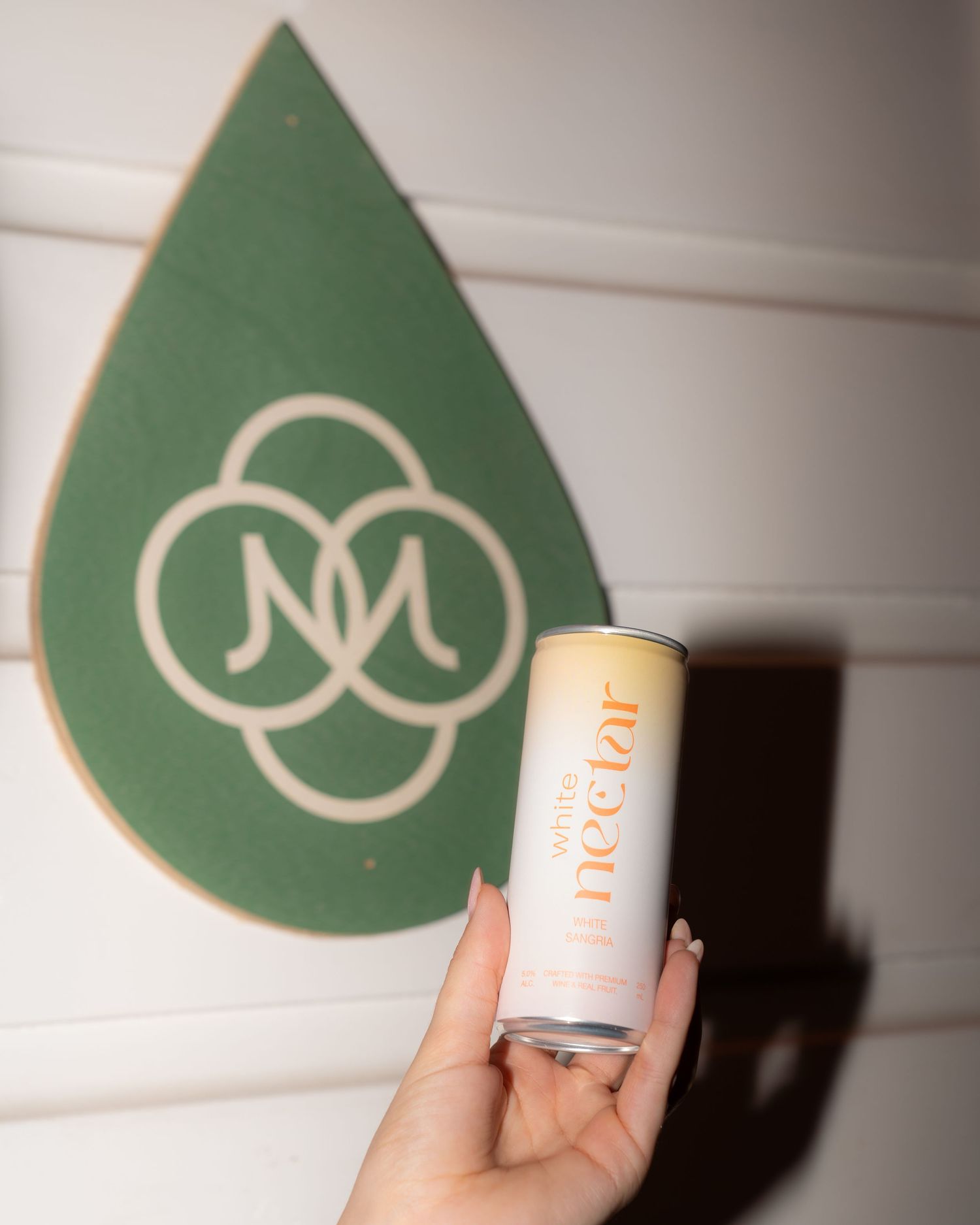 A hand holding a Nectar drink can with a green logo sign visible in the background.