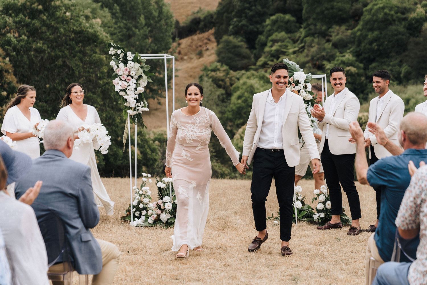 Wedding guests dance and celebrate on an outdoor grassy dance floor surrounded by hills.