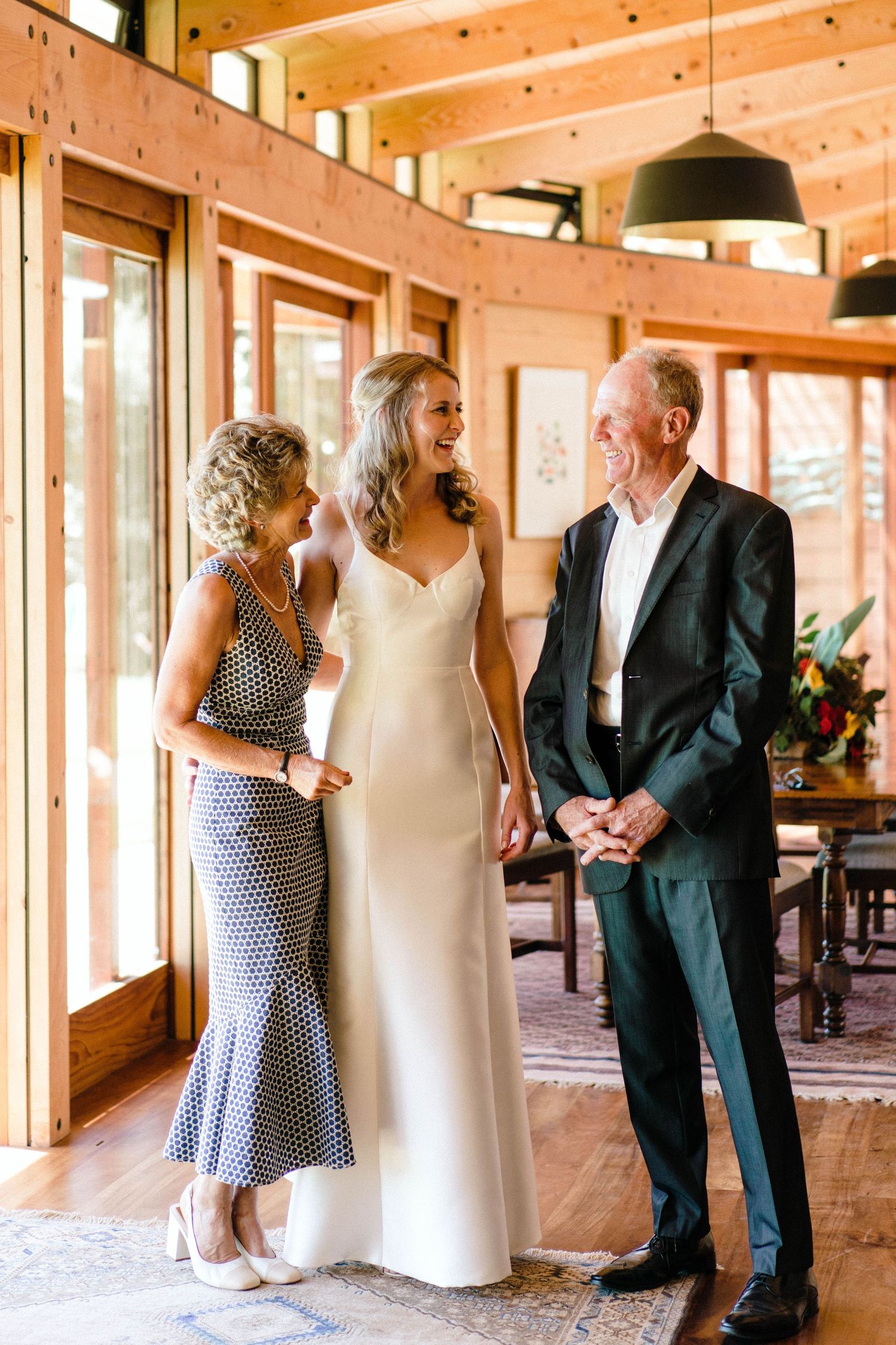 Candid moment at a wedding reception shows guests in formal attire gathering in a warm wooden interior space.