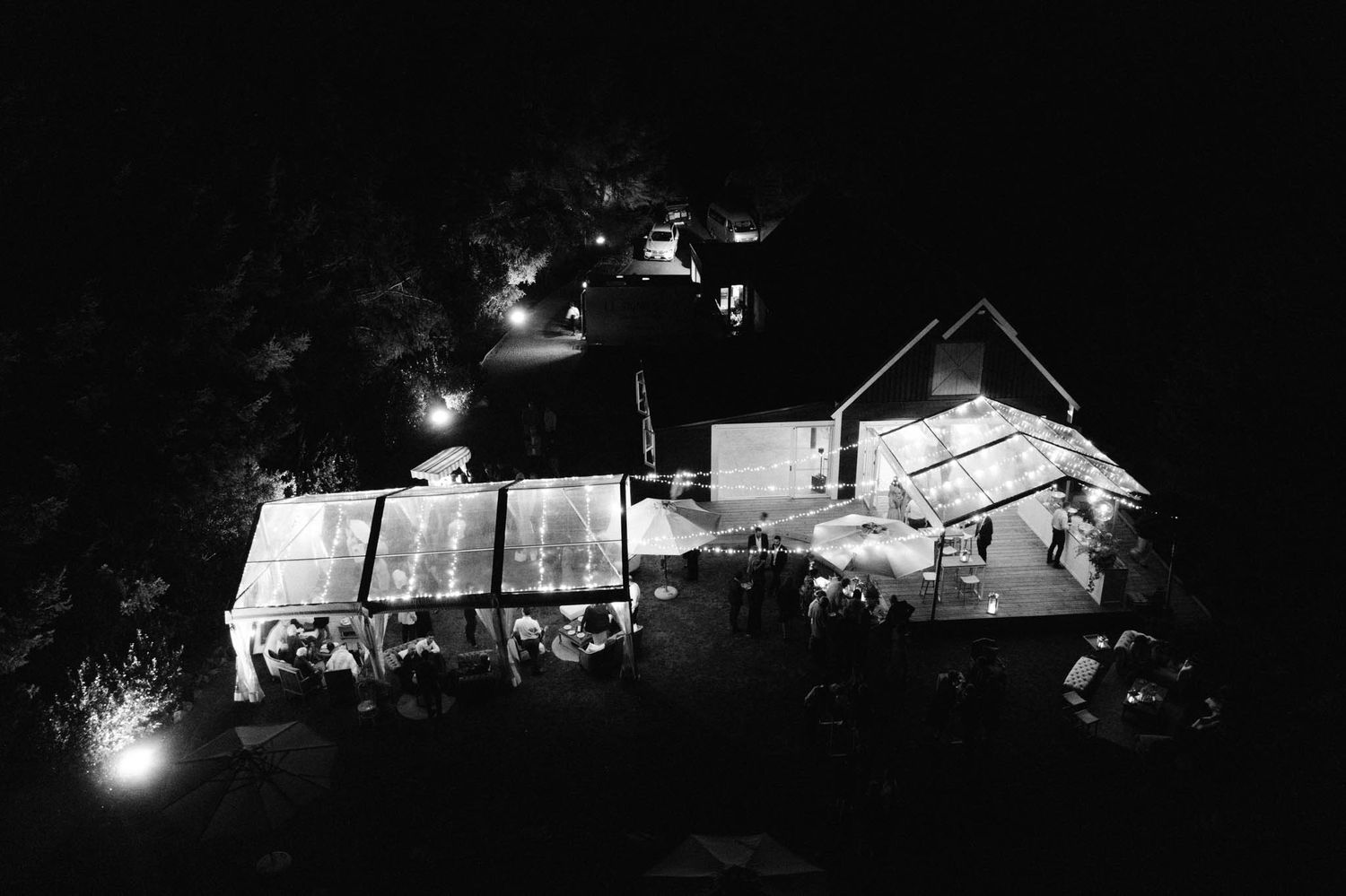 An illuminated wedding reception venue at night with tents and a house visible from above.