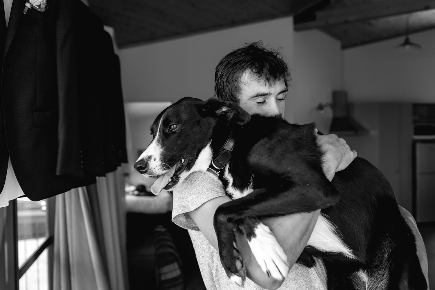 Black and white photo showing an affectionate moment between someone and their black and white dog.