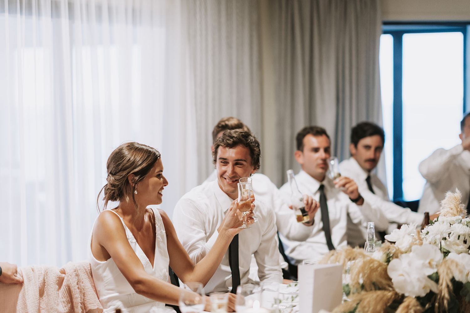 Elegant table setting at a modern wedding reception with white floral centerpieces and draping curtains.