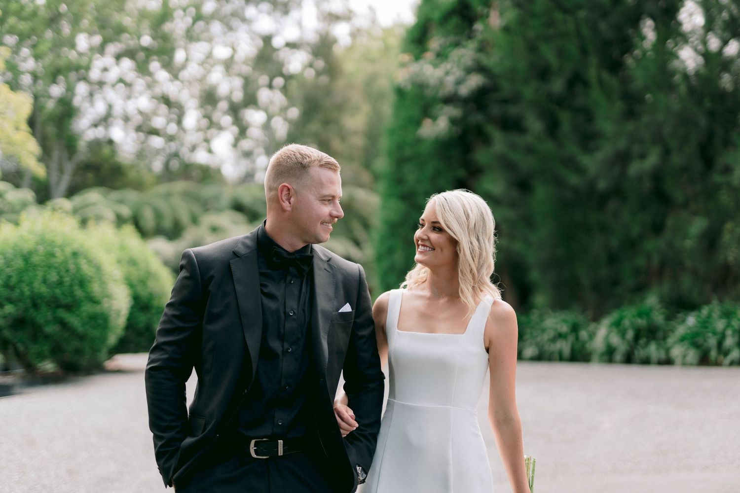 A romantic outdoor wedding photo shows a couple walking together on a garden path.
