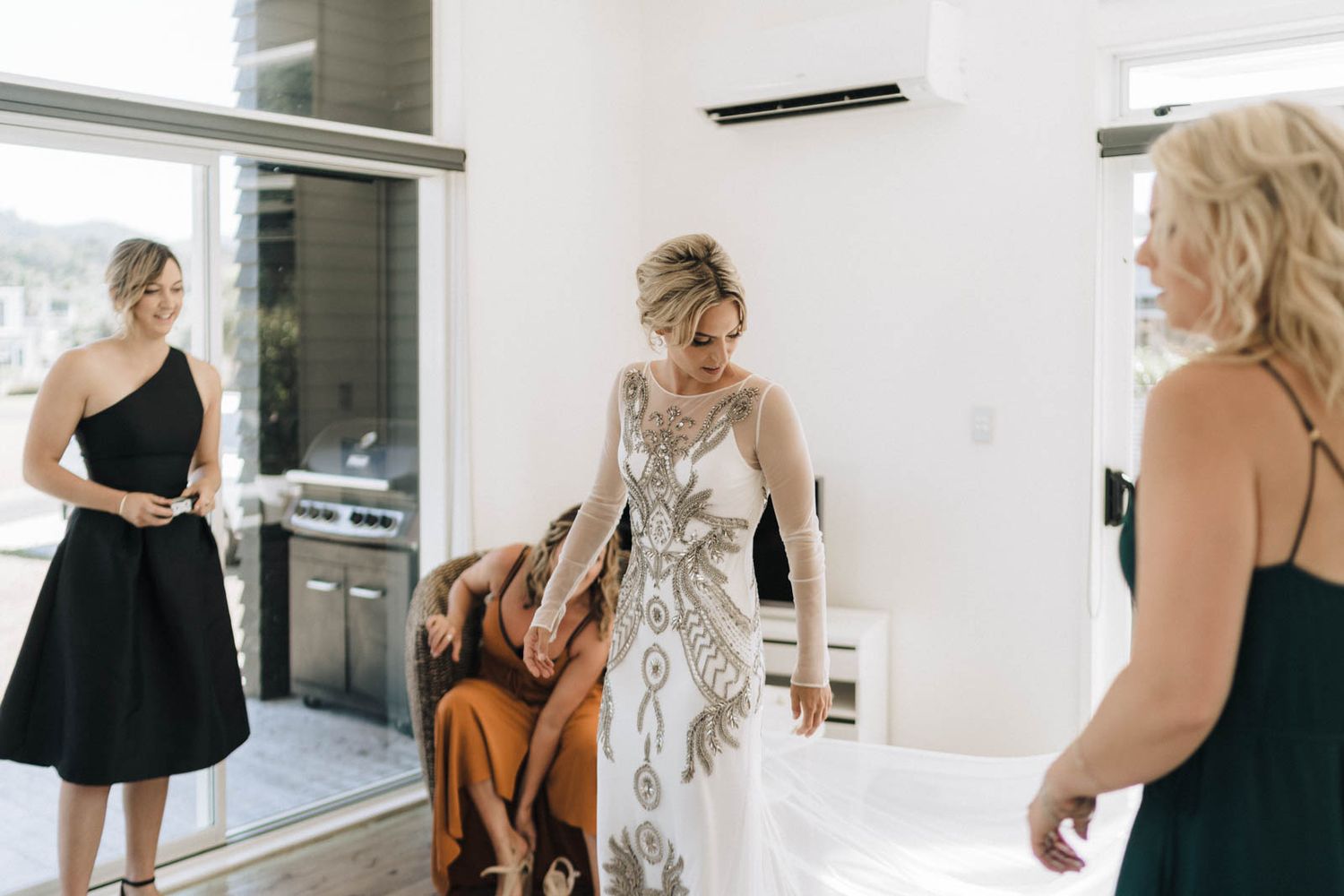 A formal gathering shows people in elegant dresses in a modern white interior setting.