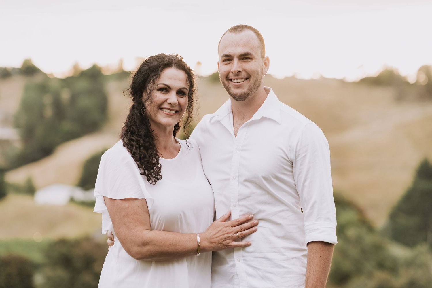 A happy couple embrace during an outdoor sunset photoshoot in a serene natural setting.