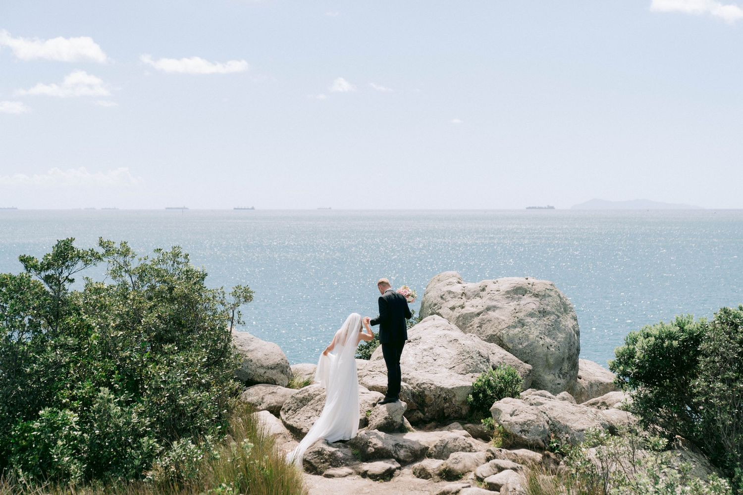 Scenic coastal wedding photos with dramatic rocky cliffs and blue ocean views.