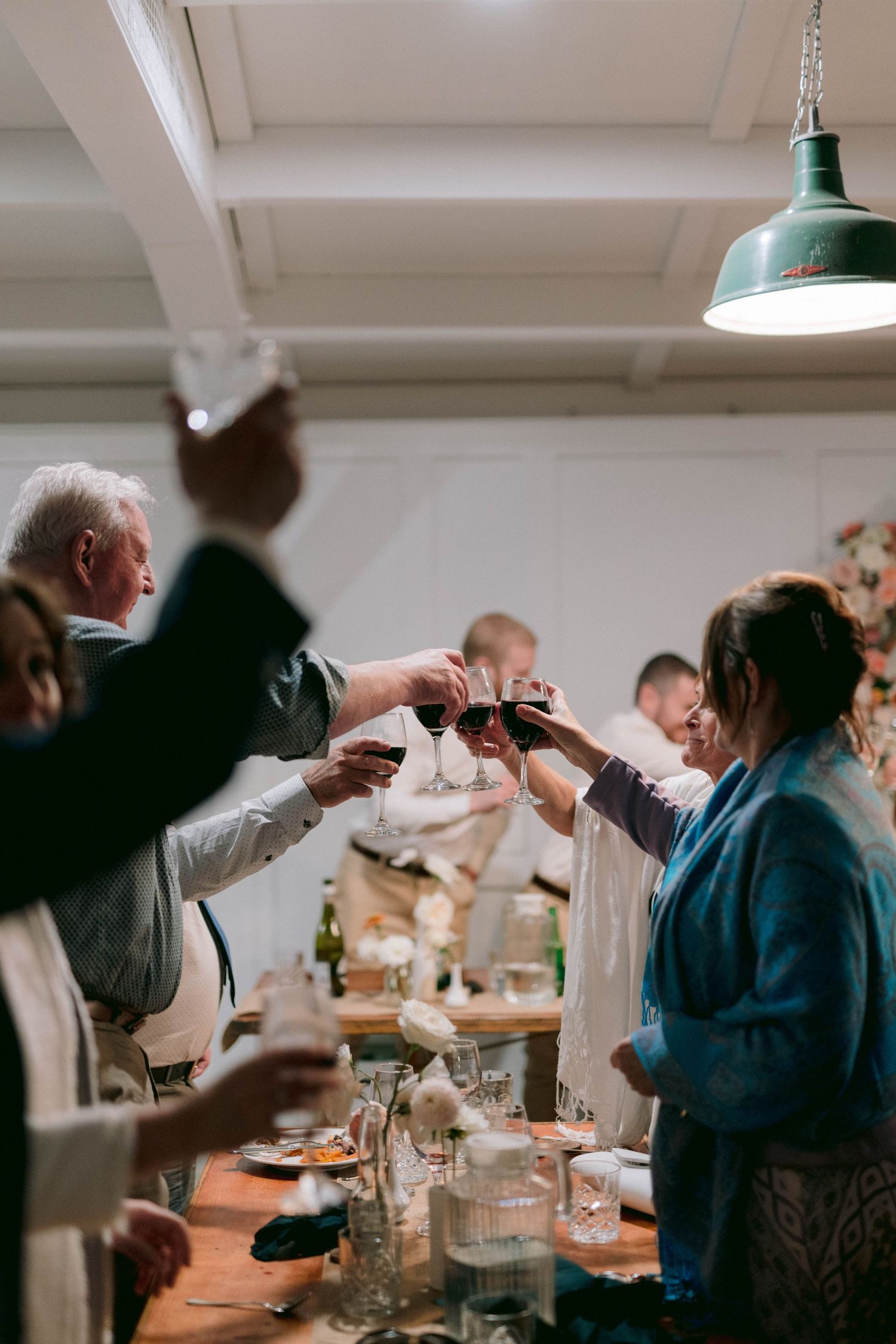 Guests raise glasses in a toast during a celebration at an indoor reception with white ceiling and industrial lighting.