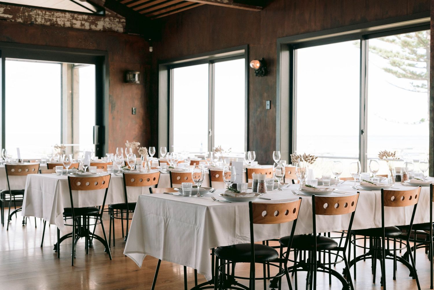 Modern restaurant interior with white tablecloths, dark chairs and large windows offering panoramic views.
