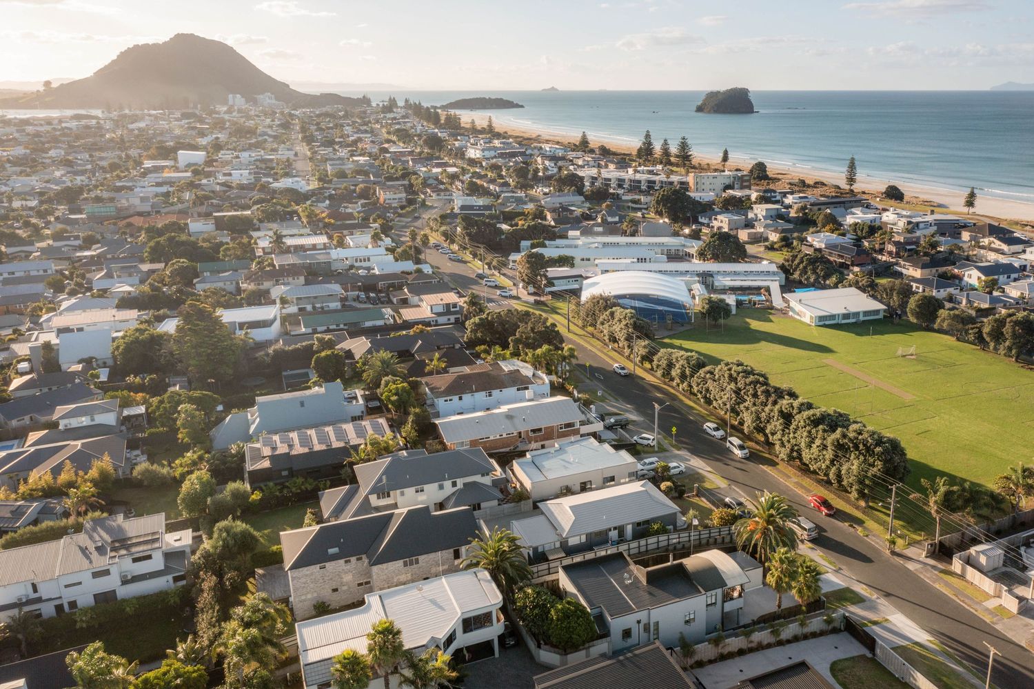 Coastal neighborhood aerial view showing luxury homes along Mount Maunganui beach with blue ocean waters.