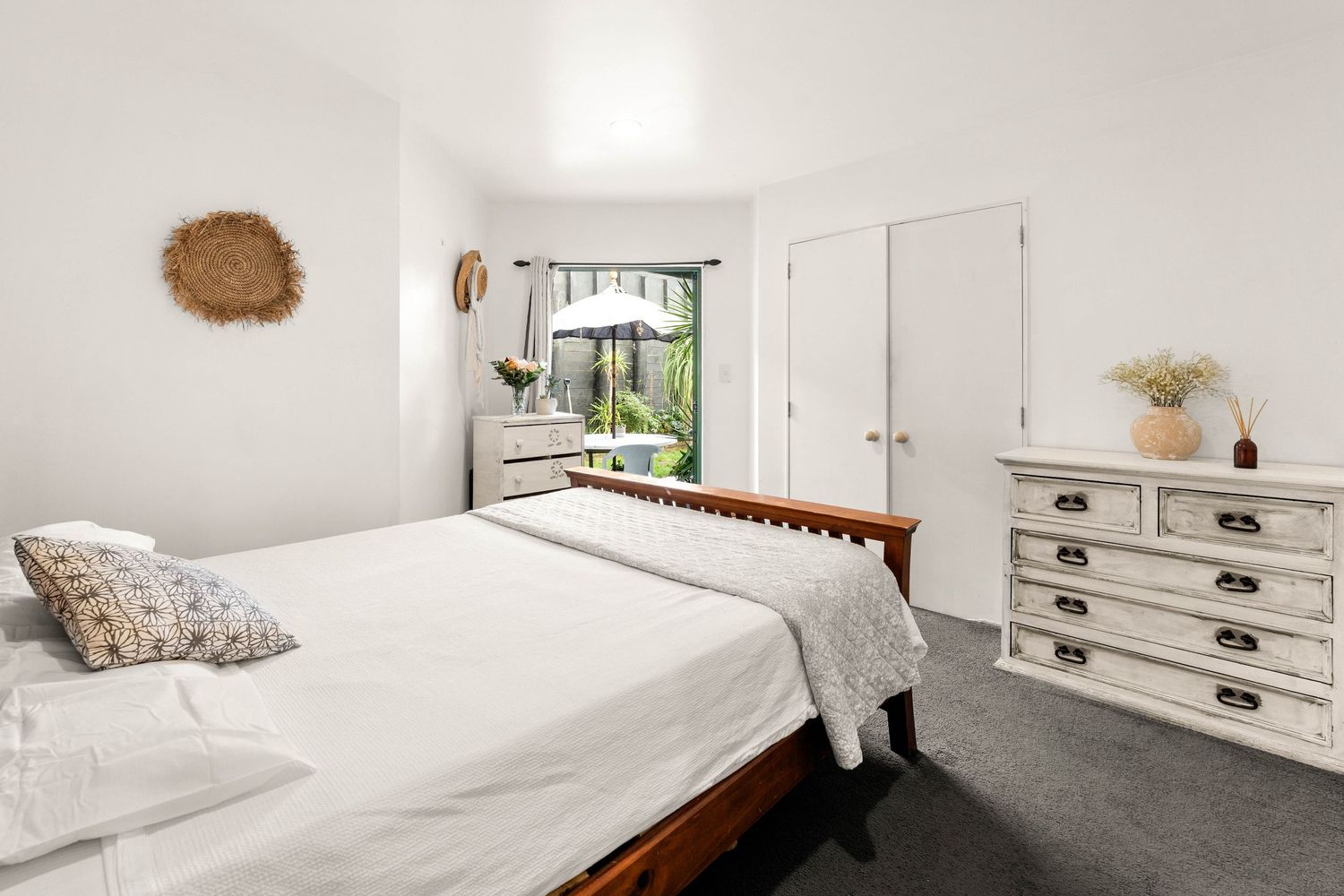 Bright bedroom with dark wood bed frame, white linens, and vintage-style white dresser.