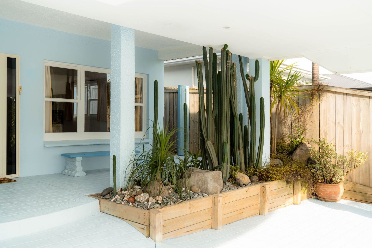 Modern white house exterior with sliding glass doors, wooden deck, and potted cacti plants creating a desert-style landscape.