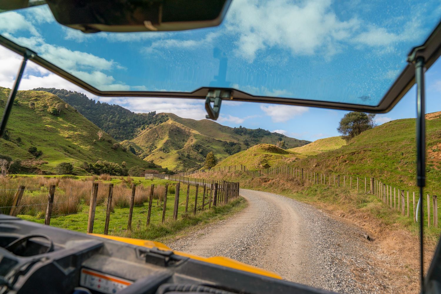 View through vehicle windshield of curving gravel road through hilly New Zealand countryside.