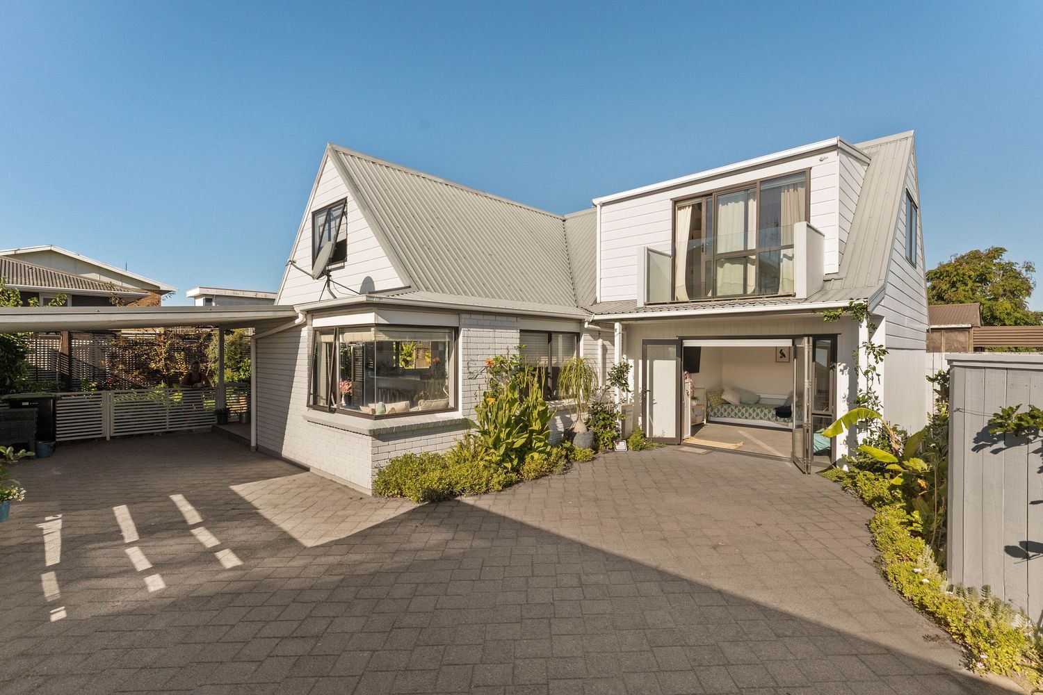 Panoramic view of a spacious wooden deck and white house exterior with landscaping.