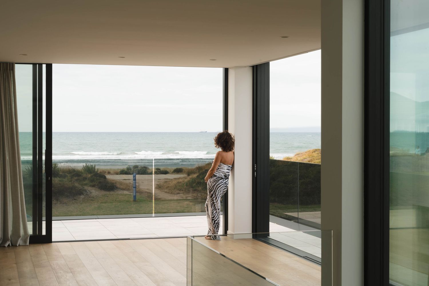Modern beach house interior with floor-to-ceiling windows overlooking the ocean.