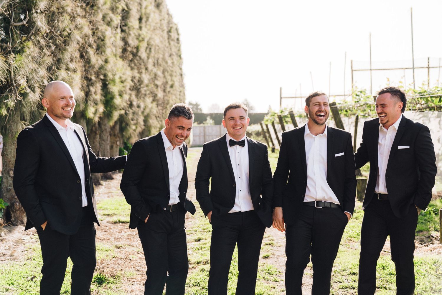 Wedding party in formal attire posing outdoors against greenery backdrop.